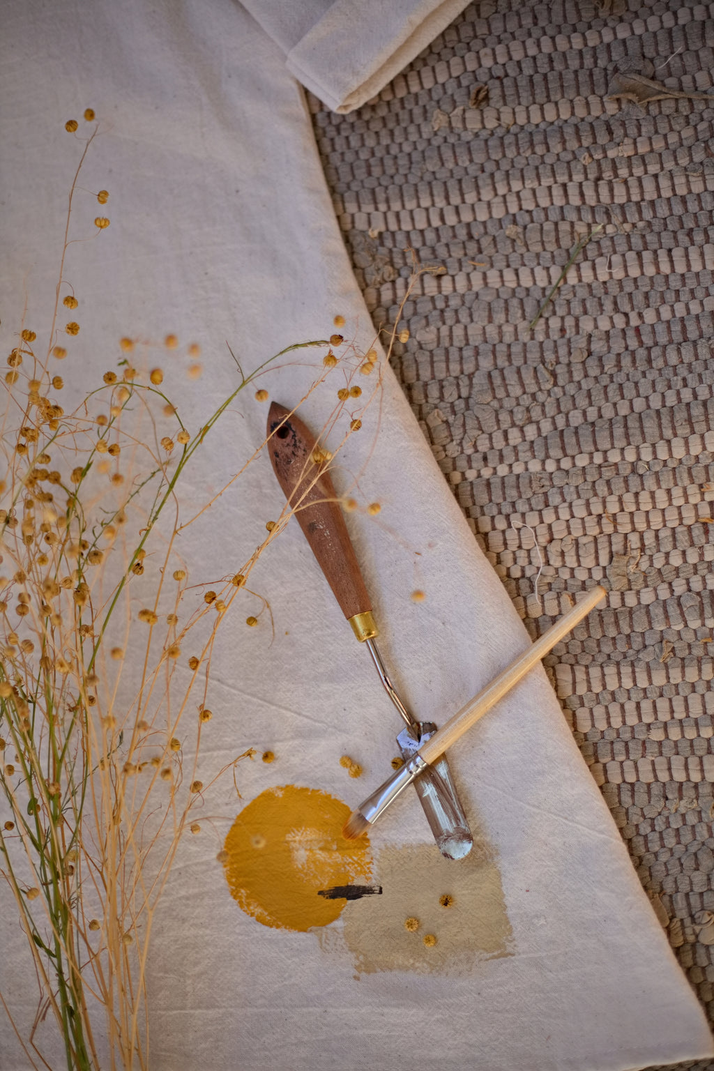 Közeli részletfotó a limitált szériás, sorszámozott No.1-es kézzel szövött khadi tunikáról, bemutatva egy egyedi sárga földpigment jelzést a stúdió festőeszközei mellett.