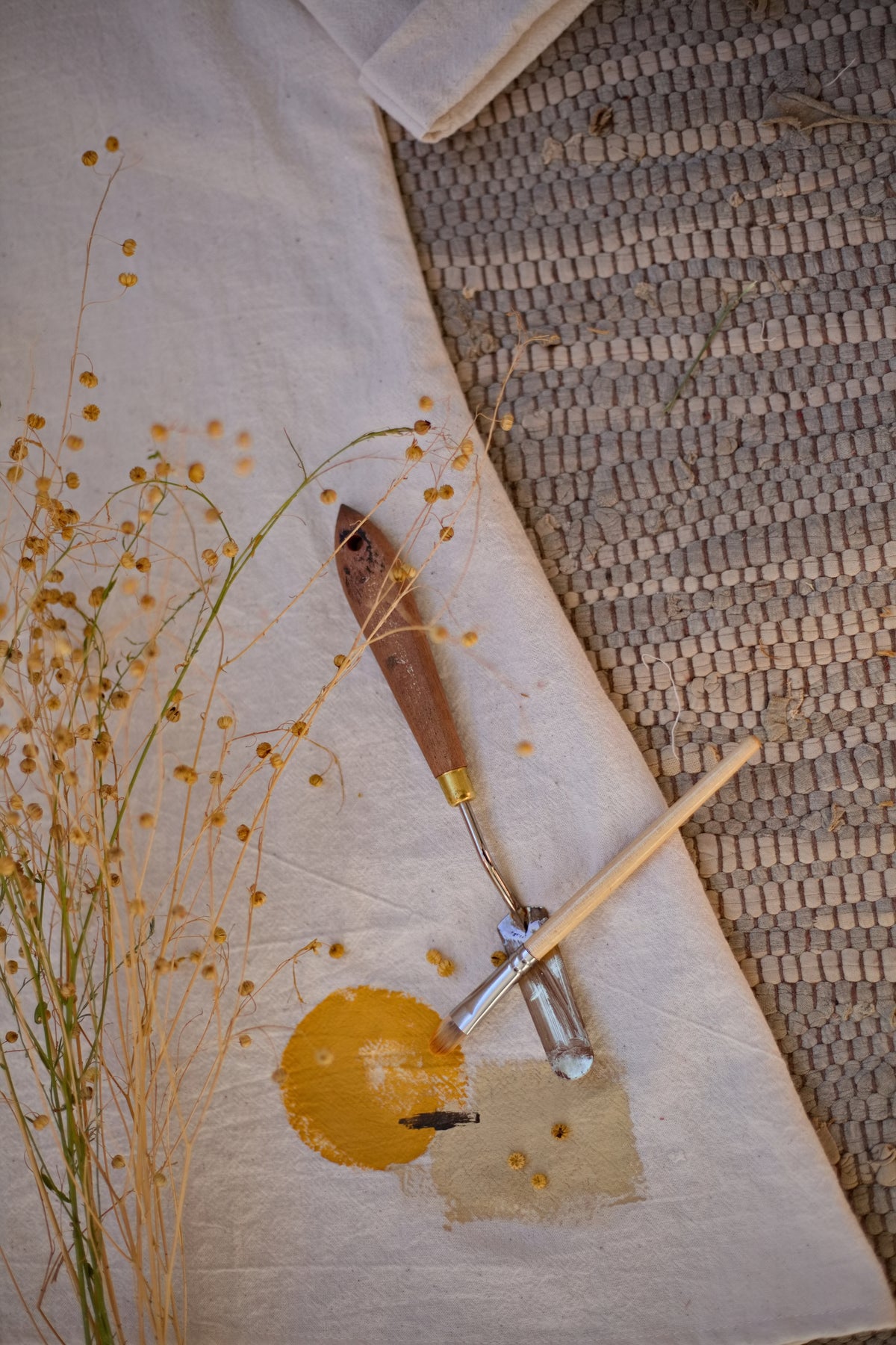 Közeli részletfotó a limitált szériás, sorszámozott No.1-es kézzel szövött khadi tunikáról, bemutatva egy egyedi sárga földpigment jelzést a stúdió festőeszközei mellett.