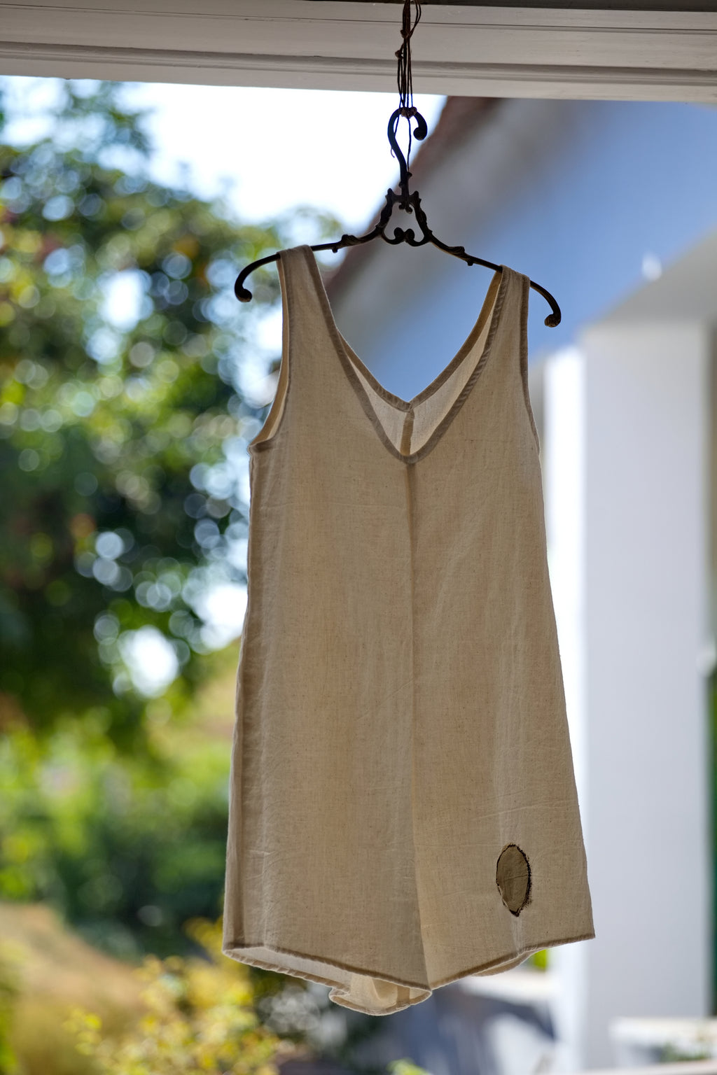 A limitált szériás, sorszámozott No.2-es kézzel szövött khadi rövid overál nyersfehér színben, egy antik hatású fa vállfára akasztva a műteremben.