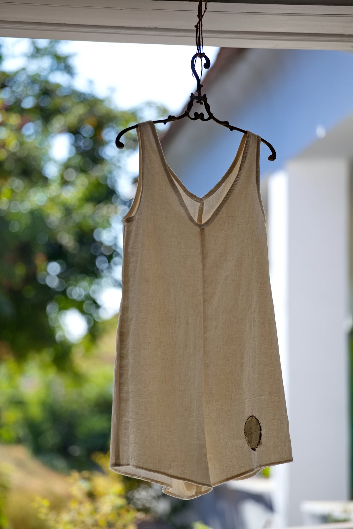 A limitált szériás, sorszámozott No.2-es kézzel szövött khadi rövid overál nyersfehér színben, egy antik hatású fa vállfára akasztva a műteremben.