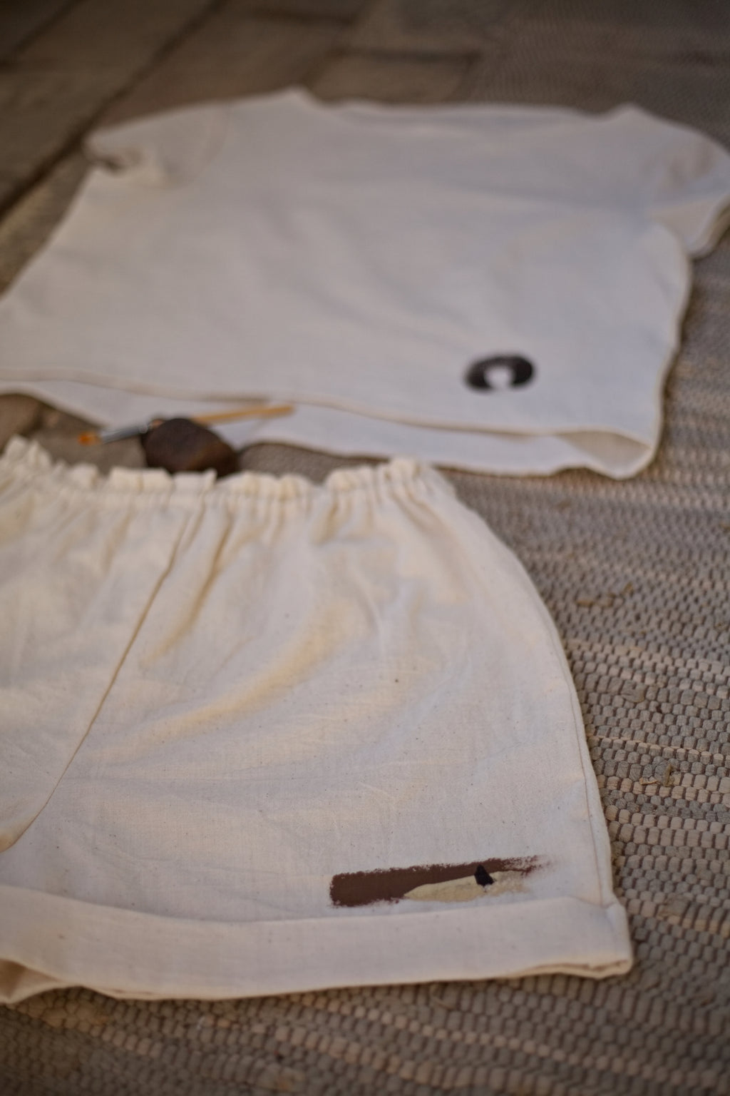 Művészi, wabi-sabi stílusú hangulatkép egy kézzel szőtt khadi rövidnadrágról és a hozzáillő felsőről, nyers földpigment részletekkel.
